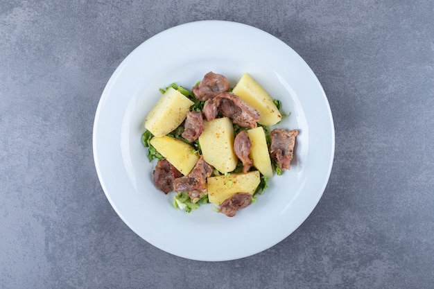 Morceaux de kebab et pommes de terre bouillies sur plaque blanche.