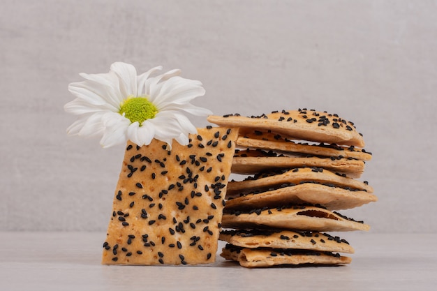 Morceaux de pain croustillant aux graines de sésame noir sur blanc avec fleur.