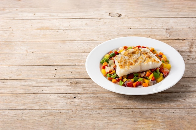 Morue grillée aux légumes dans une assiette sur une table en bois