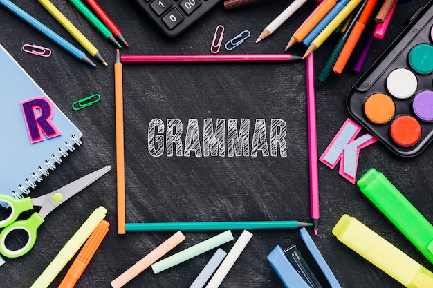 Photo gratuite mot de grammaire sur tableau avec fournitures scolaires