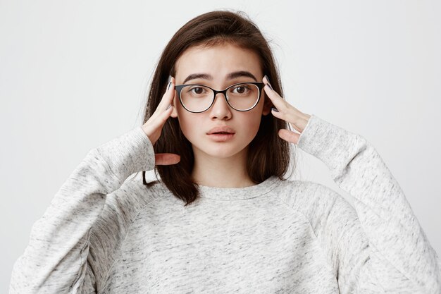 Émotionnelle femme inquiète aux cheveux noirs portant des lunettes, tenant les mains sur la tête, se sentant perplexe et frustrée après avoir quitté la maison sans avoir débranché le fer. Émotions et sentiments humains