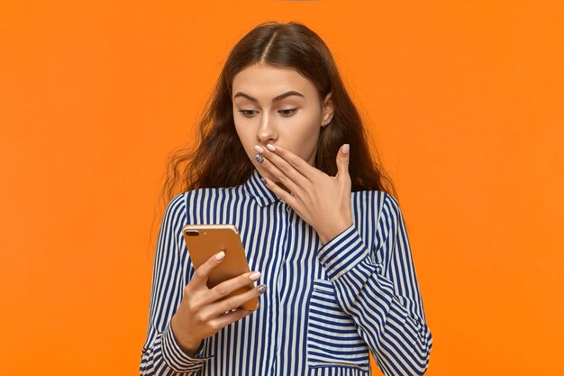 Émotionnelle jeune femme en chemise rayée couvrant la bouche ayant choqué l'expression du visage surpris