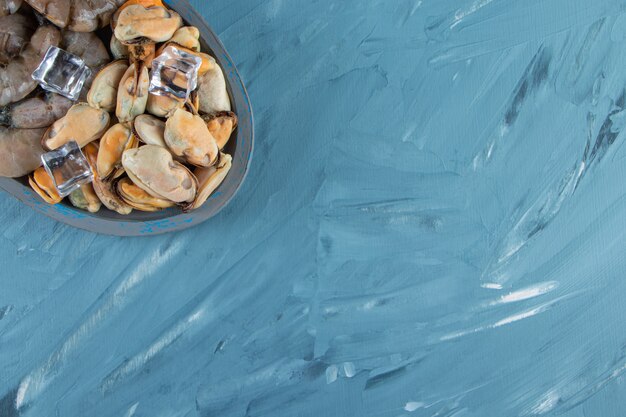 Moules, crevettes et glaçons sur une plaque en bois, sur fond de marbre.