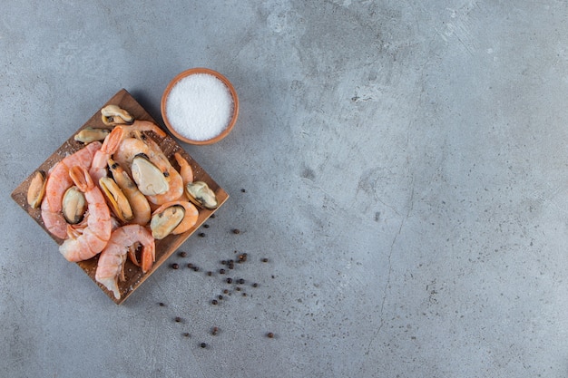 Moules et crevettes sur une planche à côté du sel , sur le fond de marbre.