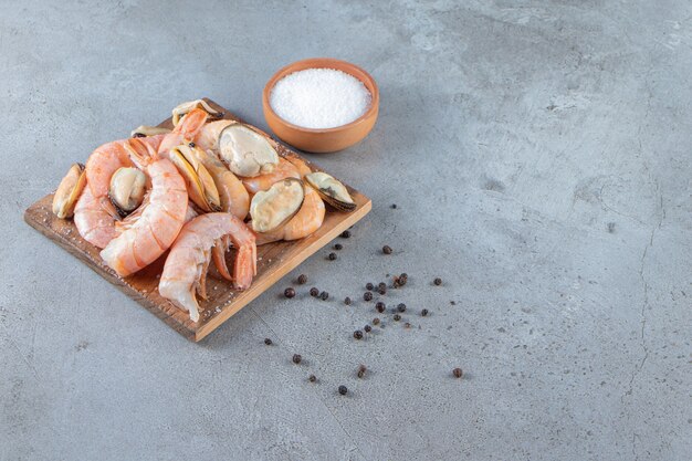 Moules et crevettes sur une planche à côté de sel, sur le fond de marbre.