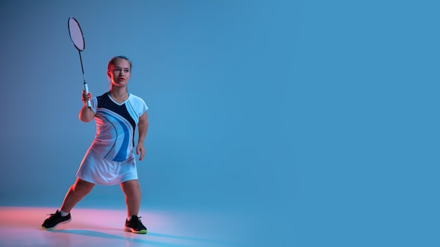 Mouvement. Belle femme naine pratiquant le badminton isolé sur bleu à la lumière du néon