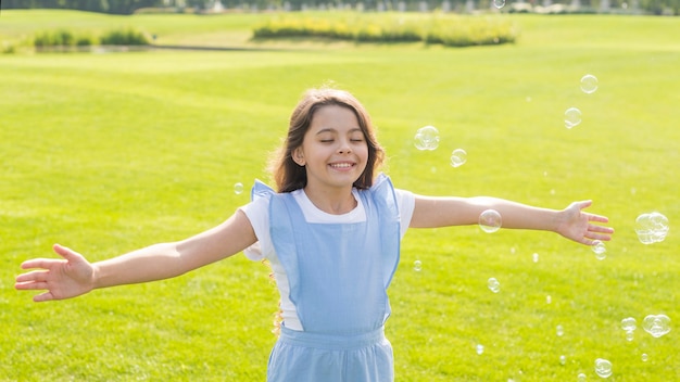 Photo gratuite moyenne fille gaie jouant avec des bulles de savon