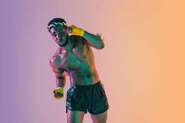 Muay thaï. Jeune homme exerçant la boxe thaï sur fond dégradé en néon.