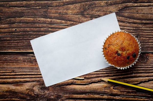 Muffin au chocolat, papier blanc vide et un crayon posé sur un plancher en bois