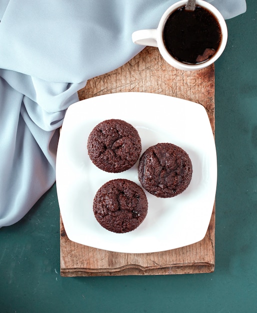 Des muffins au chocolat et une tasse de café sur un morceau de bois.