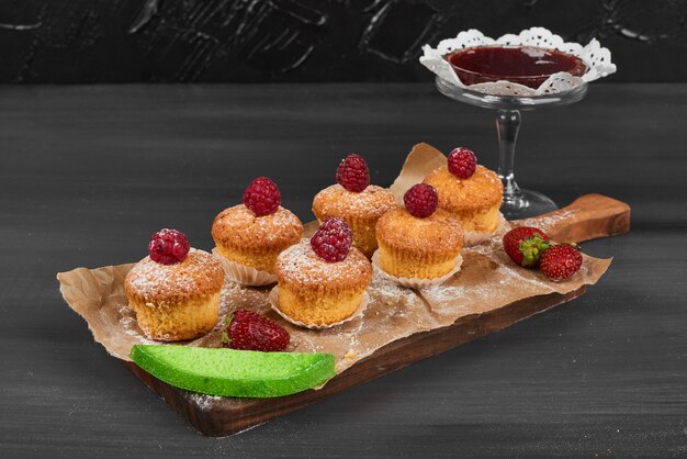 Muffins aux fruits rouges sur une planche de bois.