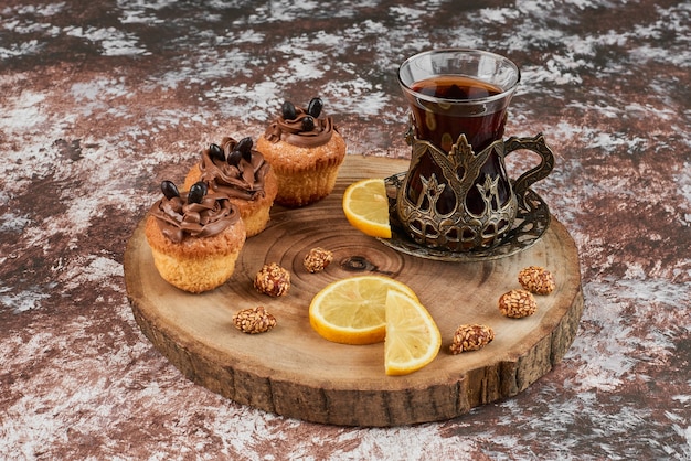 Muffins et un verre de thé sur une planche de bois.