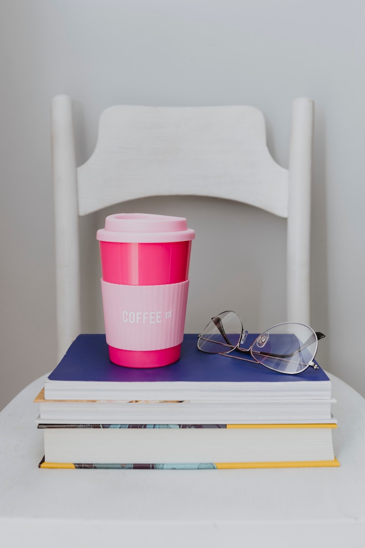 Photo gratuit mug de voyage rose sur une pile de manuels