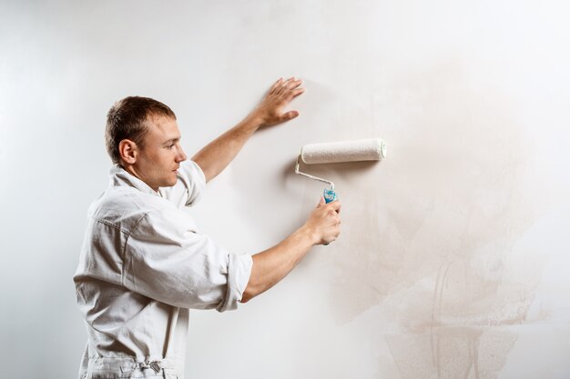 Mur de peinture de travailleur avec rouleau de couleur blanche.