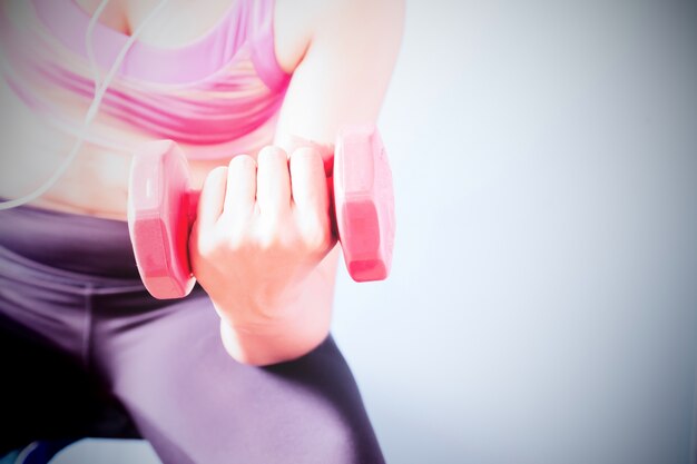 La musculation. Femme forte en soutien-gorge de sport rose exerçant avec un haltère rouge. Espace de copie