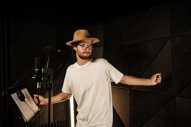 Photo gratuite musicien élégant et attrayant dansant tout en enregistrant une nouvelle chanson dans un studio de son moderne. jeune chanteur masculin chantant en studio