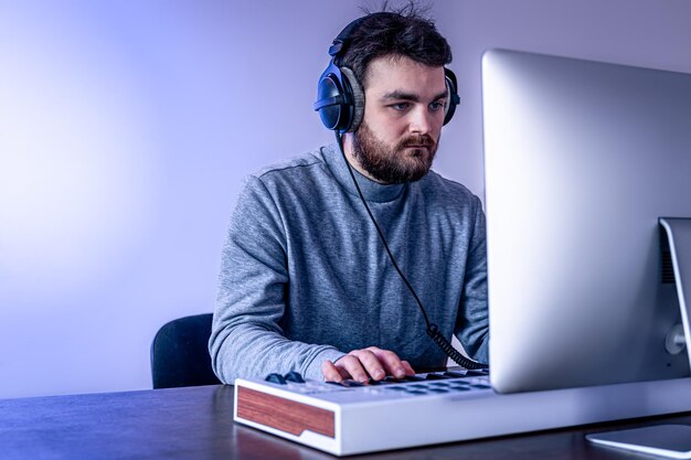 Un musicien masculin crée de la musique à l'aide d'un ordinateur et d'un clavier sur le lieu de travail d'un musicien