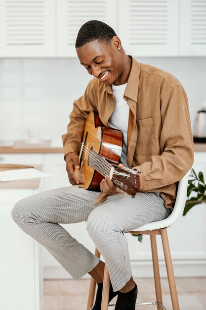 Musicien masculin Smiley à la maison sur une chaise à jouer de la guitare