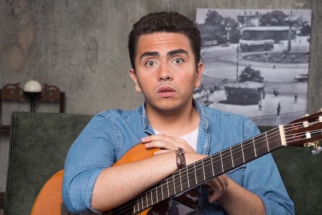 Musicien tenant une belle guitare et assis sur un canapé. Photo de haute qualité