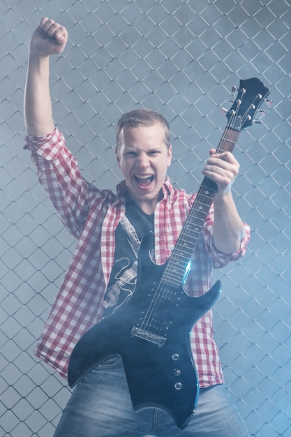 Photo gratuite la musique. jeune musicien avec une guitare sur le mur de clôture