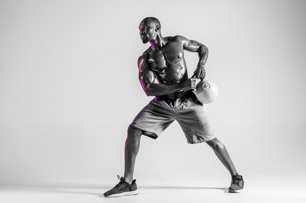 N'ayez pas peur. Formation de jeune culturiste afro-américain sur fond de studio gris. Modèle masculin célibataire musclé en tenue de sport avec le poids. Concept de sport, musculation, mode de vie sain.