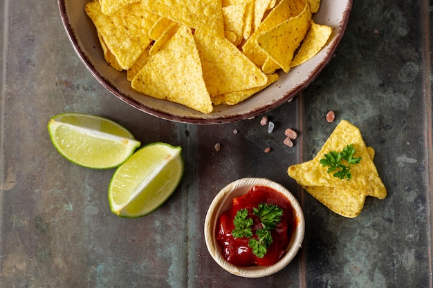 Photo gratuite nachos, sauce tomate dans un bol et citron vert en tranches sur le bureau