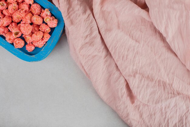 Nappe rose à côté d'un petit plateau en bois de bonbons pop-corn sur table en marbre.