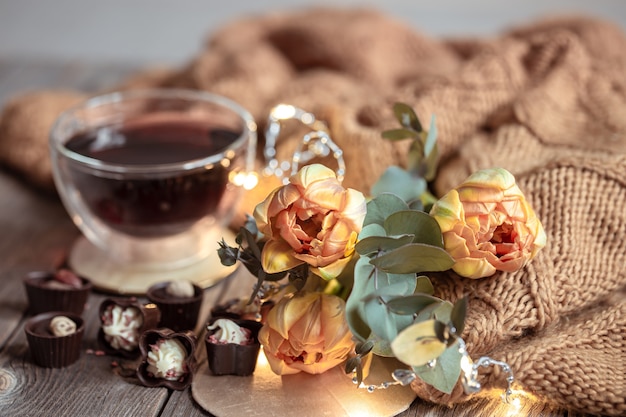 Nature morte festive avec un verre dans une tasse, des chocolats et des fleurs sur un arrière-plan flou.