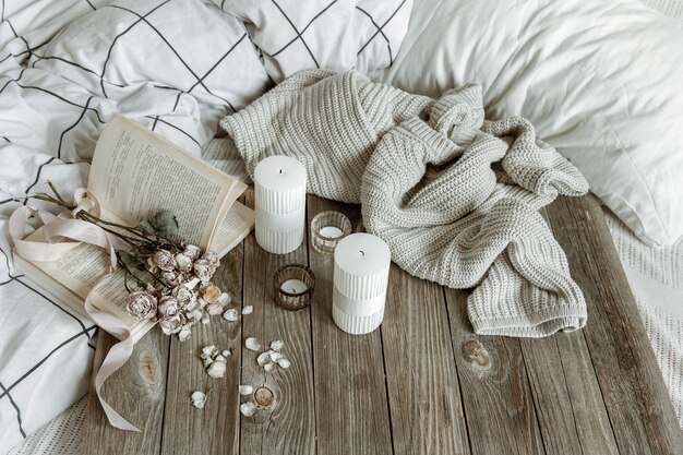 Nature morte à la maison confortable avec des bougies, un élément tricoté, un livre et des fleurs.