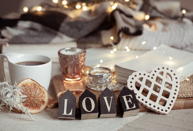 Nature morte avec le mot amour en bois, une tasse de boisson et des détails de décoration cosy sur un arrière-plan flou avec des lumières.