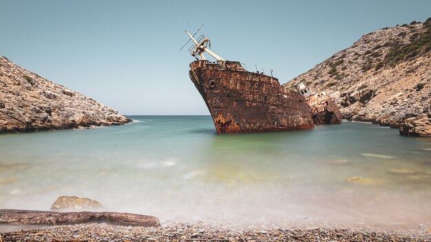 Navire rouillé abandonné dans la mer près d'énormes formations rocheuses sous le ciel clair