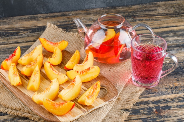 Nectarines avec boisson, morceau de sac, planche à découper sur une surface en bois et grise, vue grand angle.