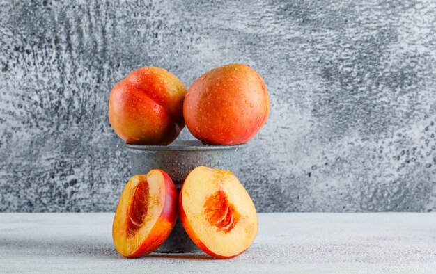 Nectarines dans un mini seau sur un mur gris sale. vue de côté.