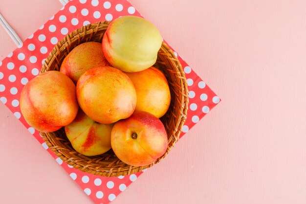 Nectarines dans un panier sur fond rose et sac en papier. pose à plat.