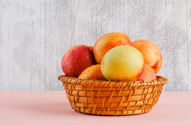 Nectarines dans un panier sur mur rose et grungy. vue de côté.