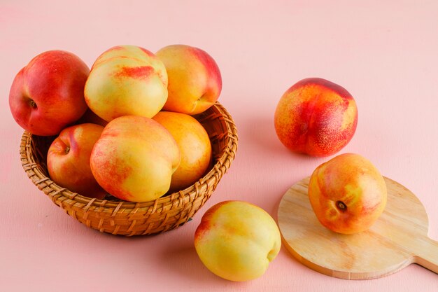 Nectarines dans un panier sur table rose et planche à découper. vue grand angle.