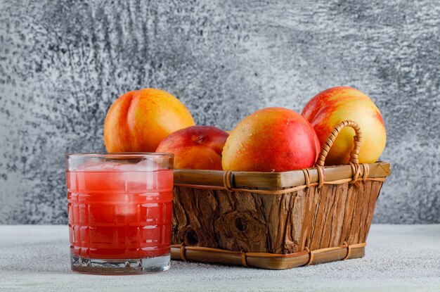 Nectarines dans un panier avec vue de côté de jus sur un mur sale