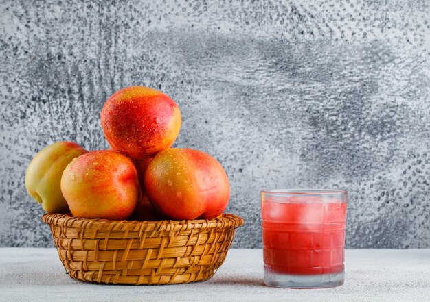 Nectarines avec du jus dans un panier sur fond grungy et blanc, vue latérale.