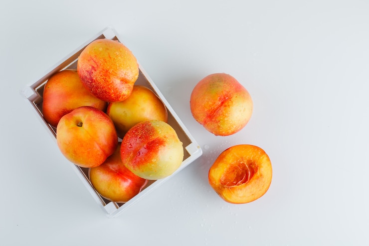 Photo gratuit nectarines mûres dans une boîte en bois sur table blanche, mise à plat.