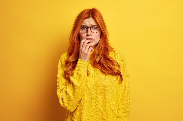 Nerveuse jeune femme rousse semble inquiète se sent gênée fronce les sourcils Le visage porte des lunettes optiques et un pull.