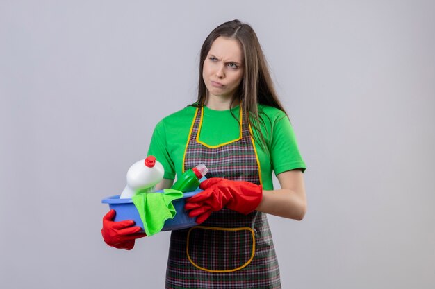 Nettoyage triste jeune fille en uniforme dans des gants rouges tenant des outils de nettoyage sur fond blanc isolé