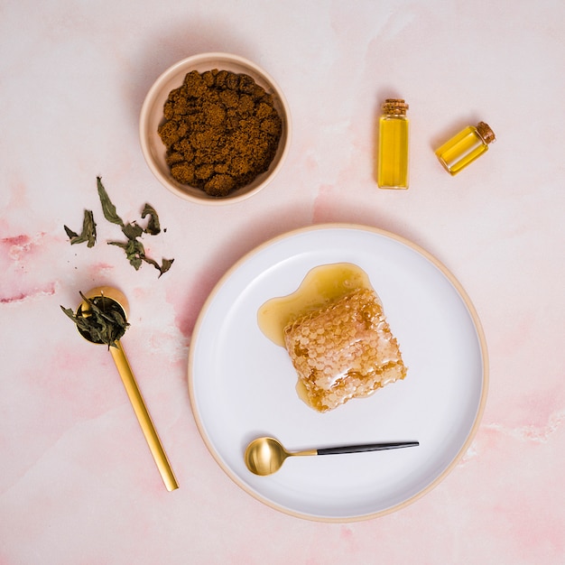 Nid d&#39;abeille et miel sur une assiette en céramique avec des produits cosmétiques sur fond texturé rose