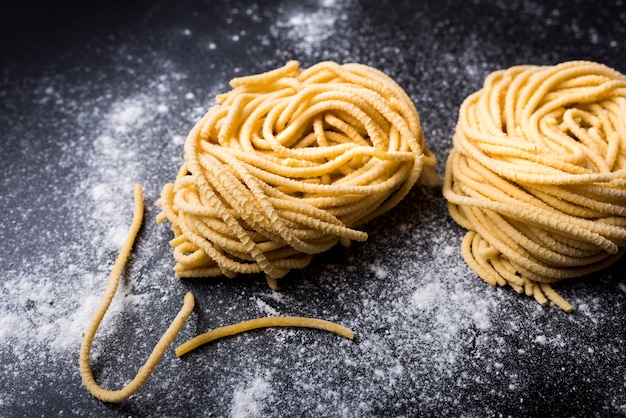 Photo gratuite nid de pâtes capellini maison crues avec de la farine sur fond noir