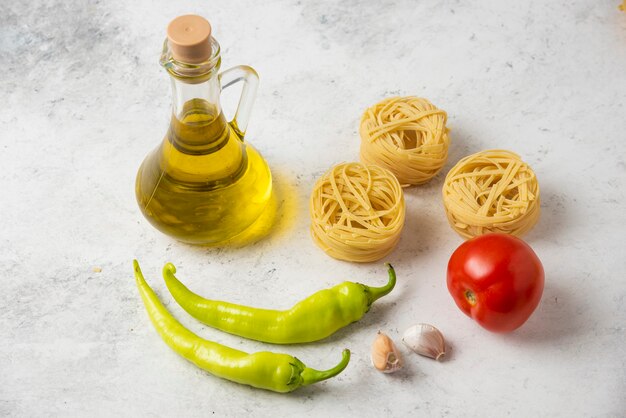 Nids de pâtes crues, bouteille d'huile d'olive et légumes sur tableau blanc.