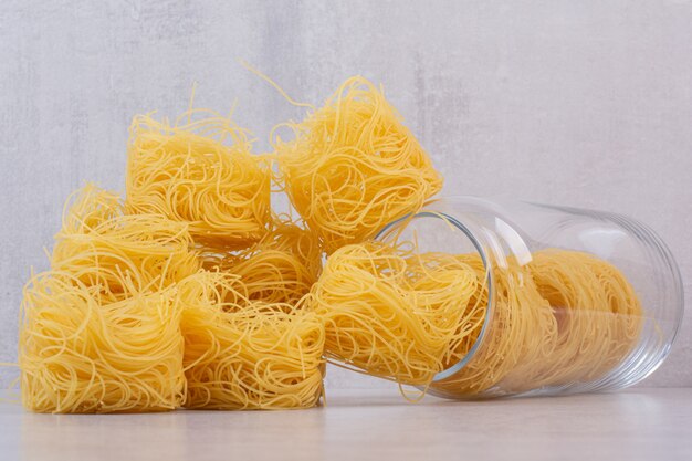 Nids de spaghetti non cuits sur la surface de la pierre avec bocal en verre