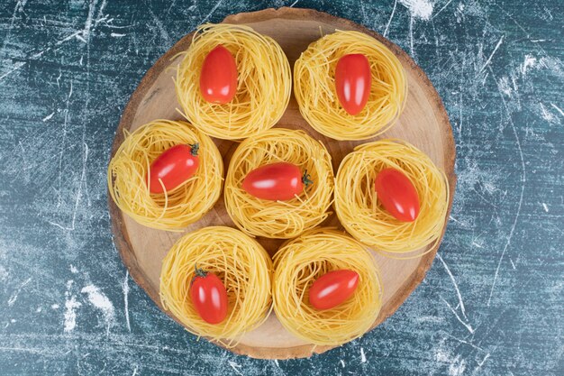 Nids de spaghettis crus avec des tomates sur planche de bois. Photo de haute qualité