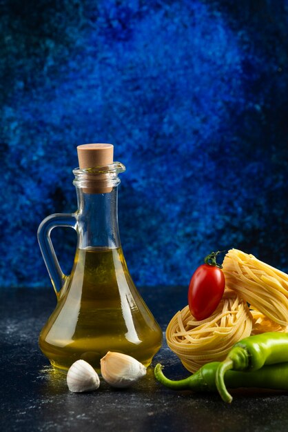 Nids de tagliatelles, huile et légumes sur table en marbre.