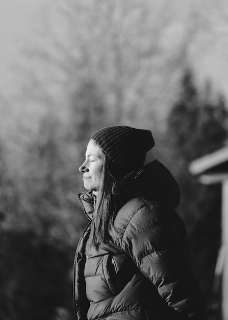 Niveaux de gris du profil latéral d'une fille aux yeux fermés sous la lumière du soleil sur un arrière-plan flou