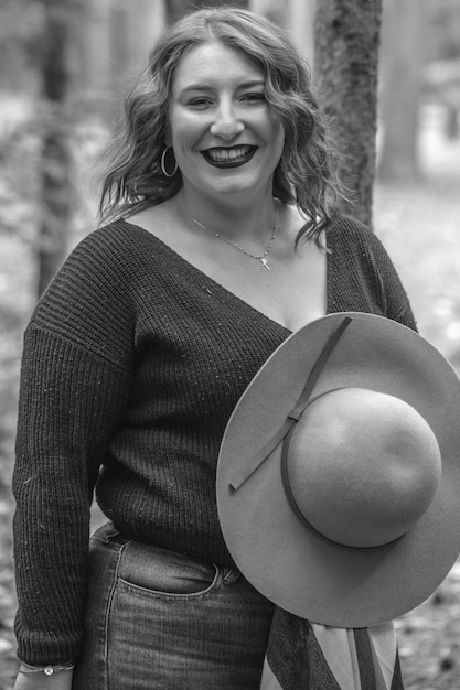 Photo gratuite niveaux de gris d'une femme souriante avec un chapeau dans une forêt