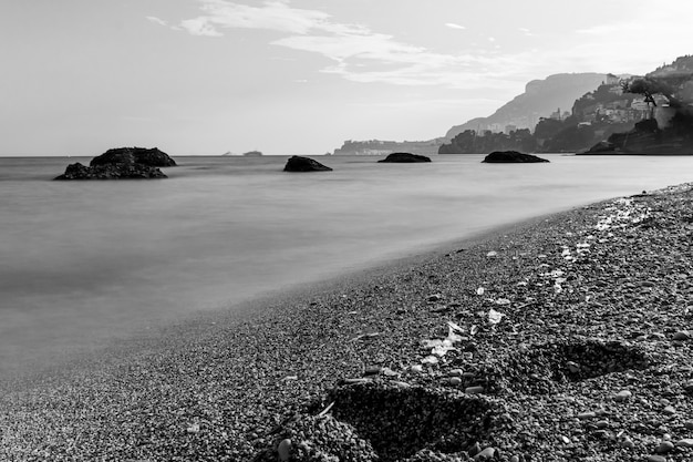 Niveaux de gris d'une plage couverte de pierres entourée par la mer avec des montagnes